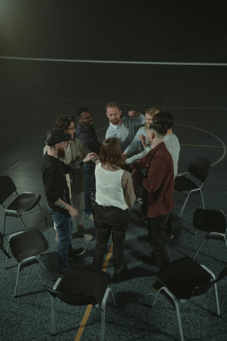 A group of adults engaged in a team-building activity indoors with chairs arranged in a circle.